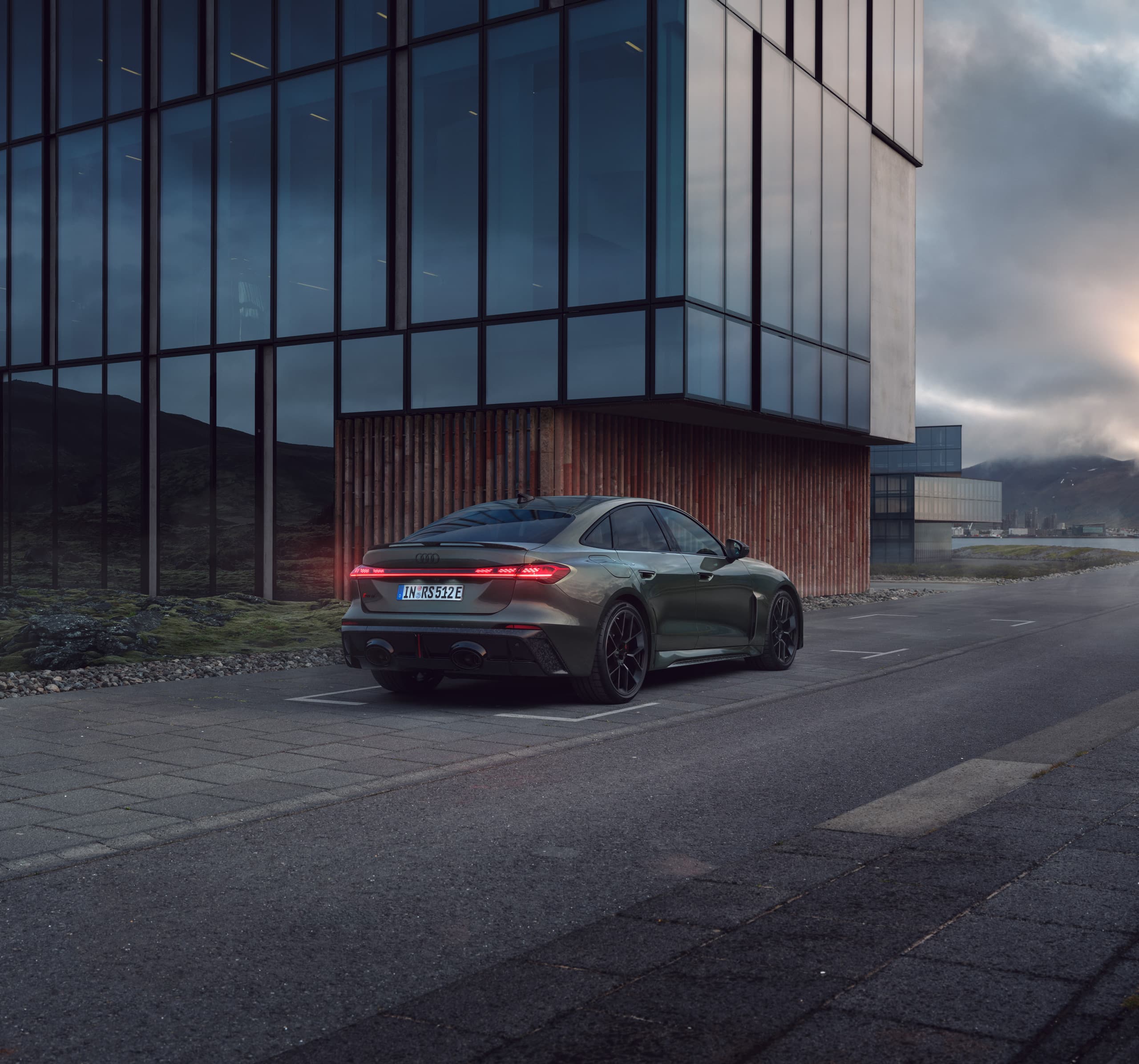 Mørkegrøn Audi RS 5 bagfra foran moderne bygning ved solnedgang