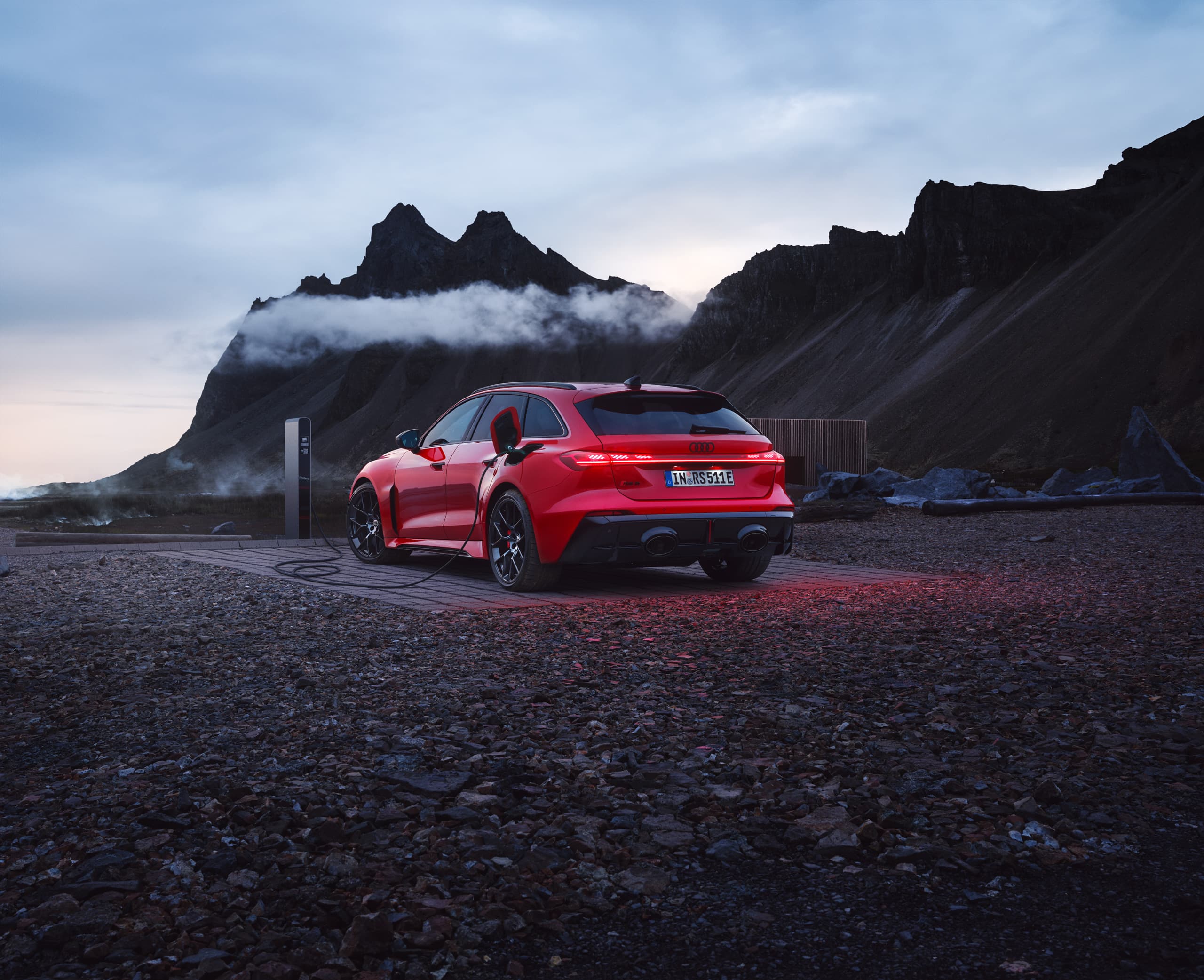 Rød Audi RS 5 Avant bagfra parkeret ved klippekyst med bjerge